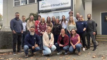 Group staff photo in front of school and their sign