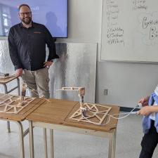 Two female students working their constructed design in Engineering class, male teacher stands and watches